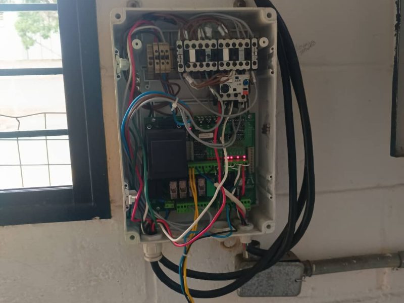 Caja plástica pequeña con la tarjeta de control y los contactores amontonados, cables cruzados y sin canalizar.