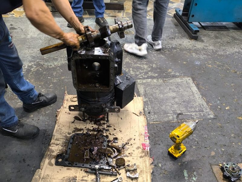 Compresor semihermético abierto en el taller, con el cigüeñal fuera y las piezas sobre un cartón.