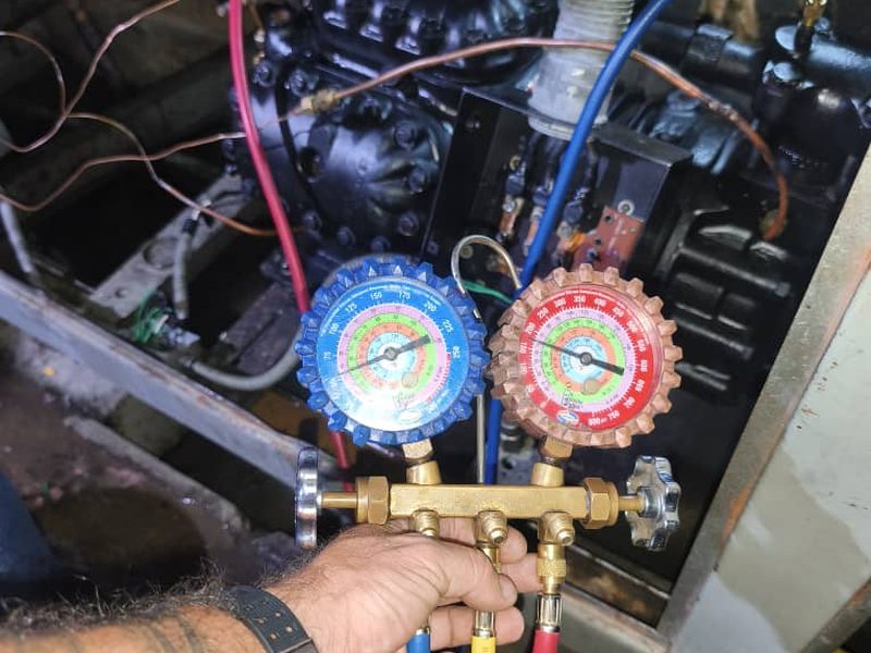 Un técnico sostiene un juego de manómetros conectado al compresor ya en marcha.