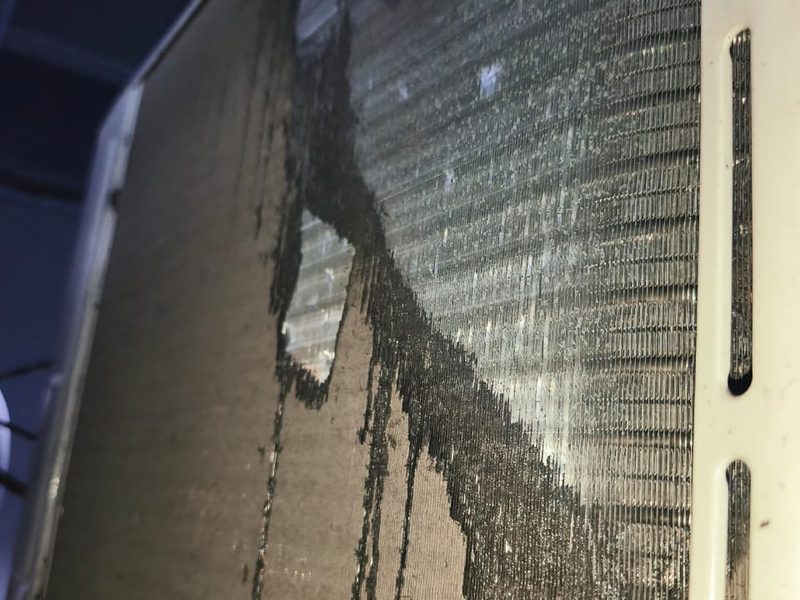 Serpentín de una evaporadora con la suciedad negra corriendo entre las aletas mientras se lava a presión.