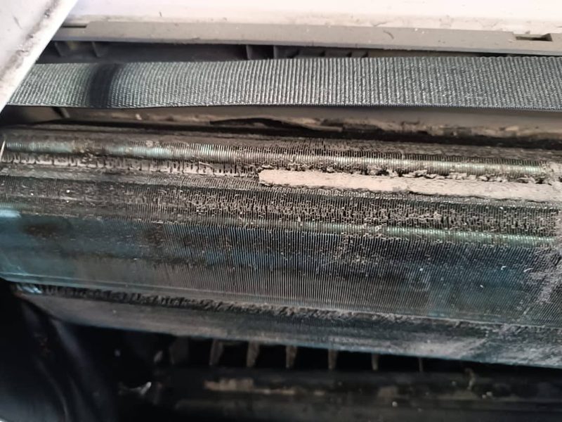 Serpentín de evaporadora con una capa gris de polvo y suciedad entre las aletas.