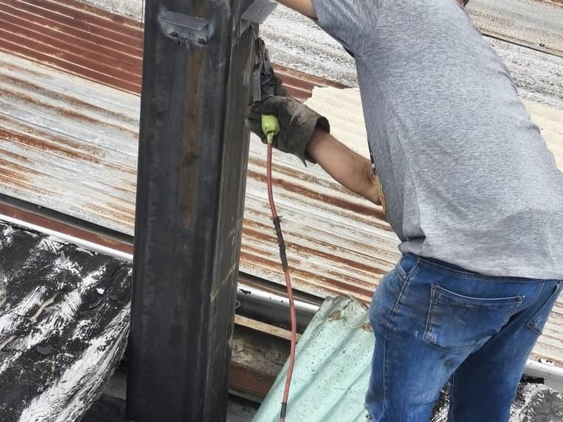 Un técnico con careta y guantes de soldar trabaja sobre una viga metálica en un techo.